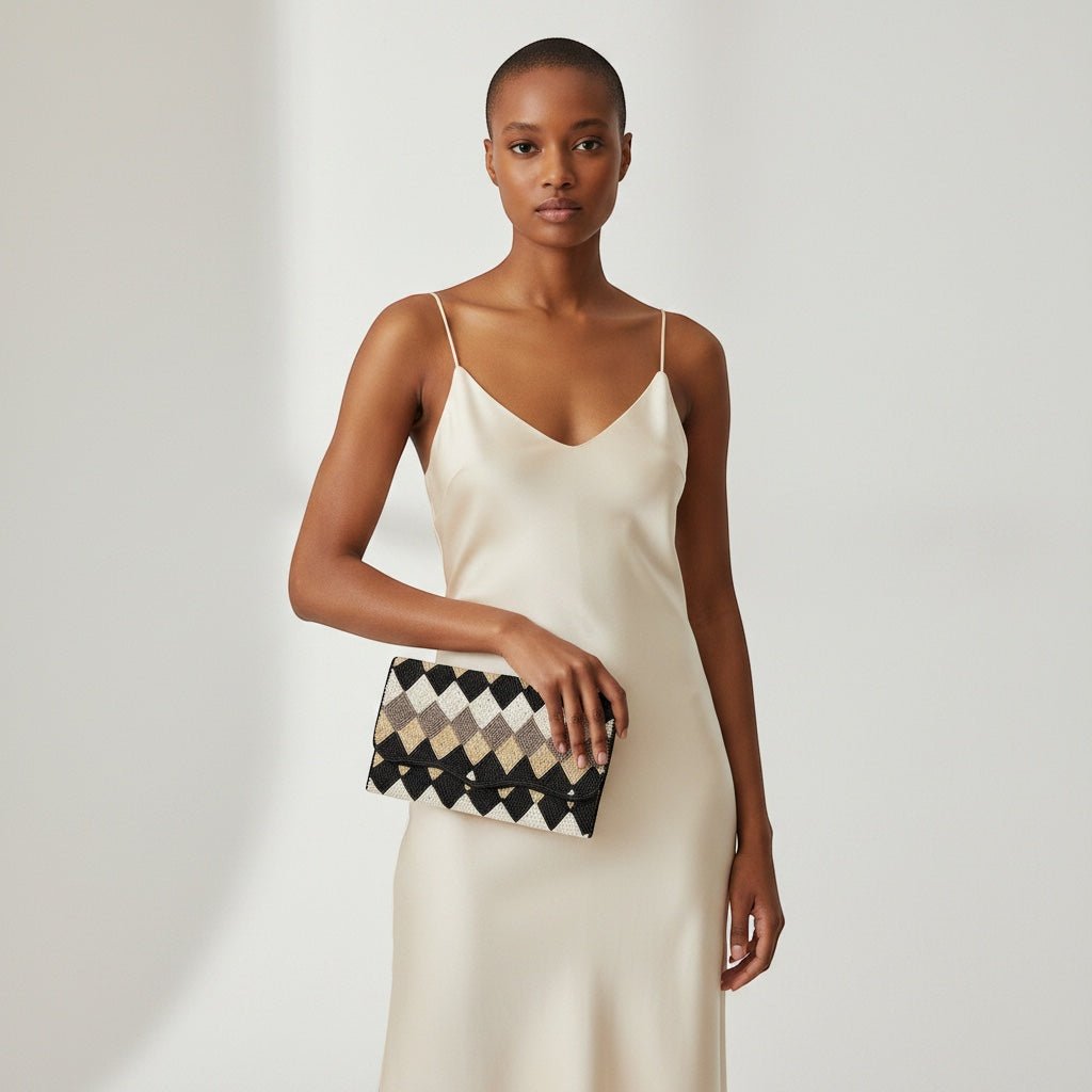JOYCO Aurora clutch with black, white, and gold geometric embroidery held by a model in a cream silk slip dress.