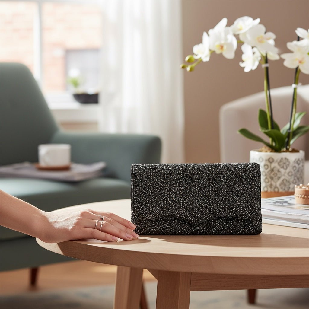 JOYCO Black Orchid embroidered clutch with intricate beadwork on a wooden table next to a white orchid plant