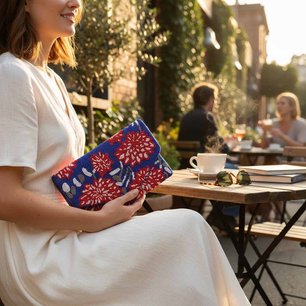 JOYCO Bluma clutch featuring intricate blue and red floral embroidery held by a woman in a white dress at a cafe.