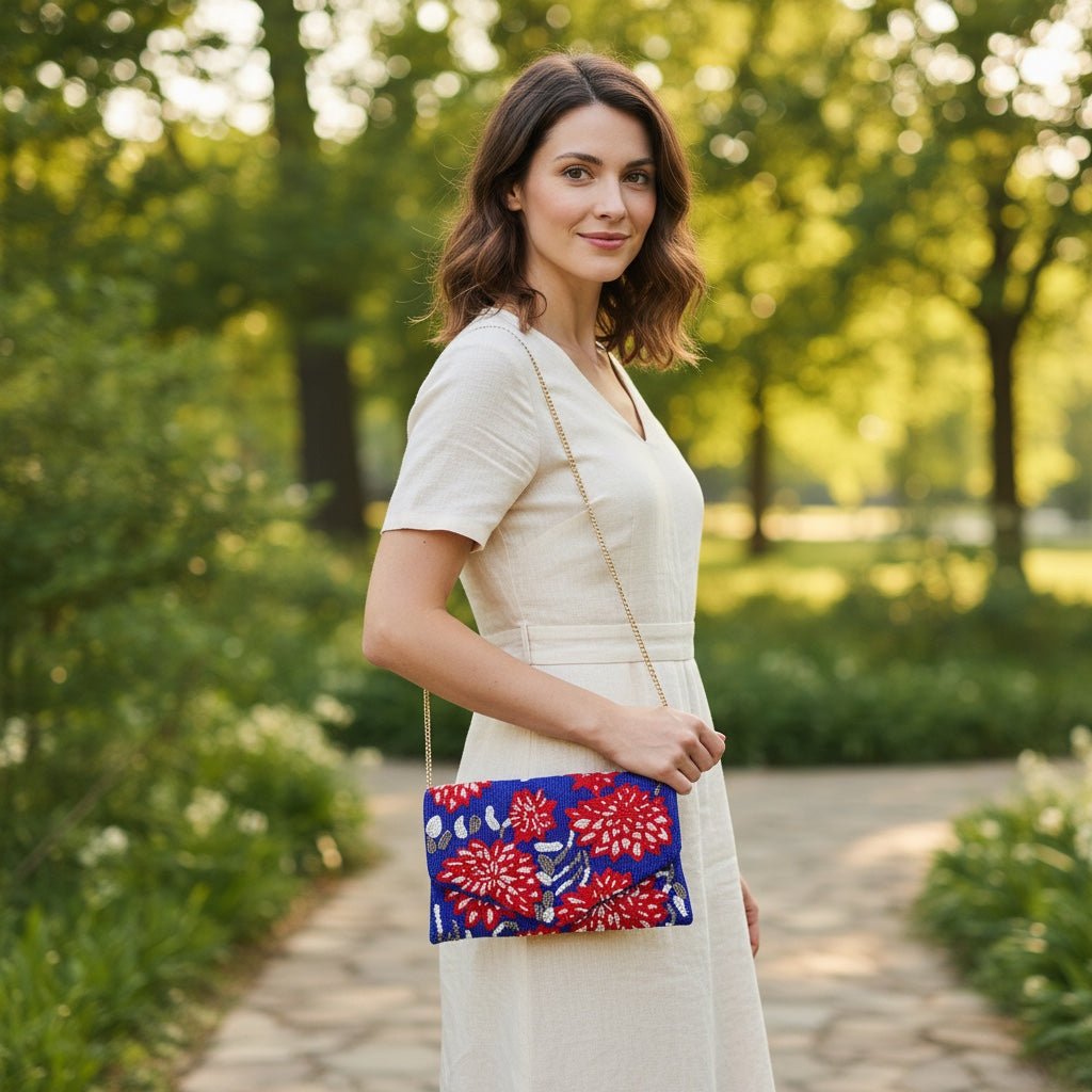 JOYCO Bluma embroidered clutch with red and white floral patterns, worn as a crossbody bag by a woman in a park.