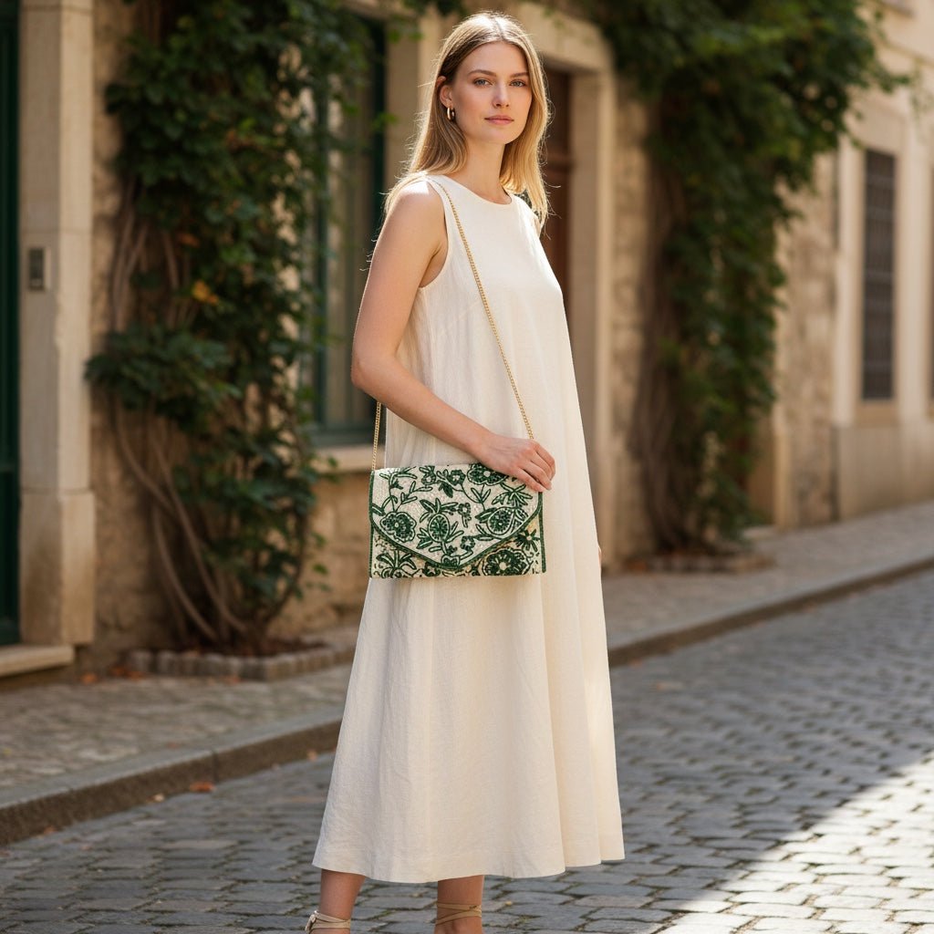 JOYCO emerald green embroidered clutch with gold chain strap held by a woman in a cream linen dress on a cobblestone