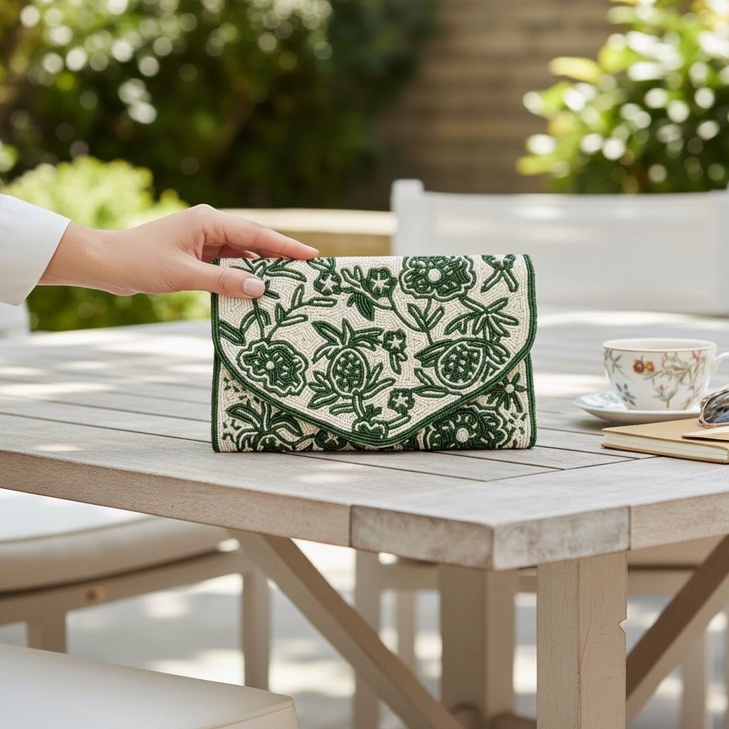 JOYCO emerald green clutch with intricate floral embroidery and gold accents held on a wooden outdoor table