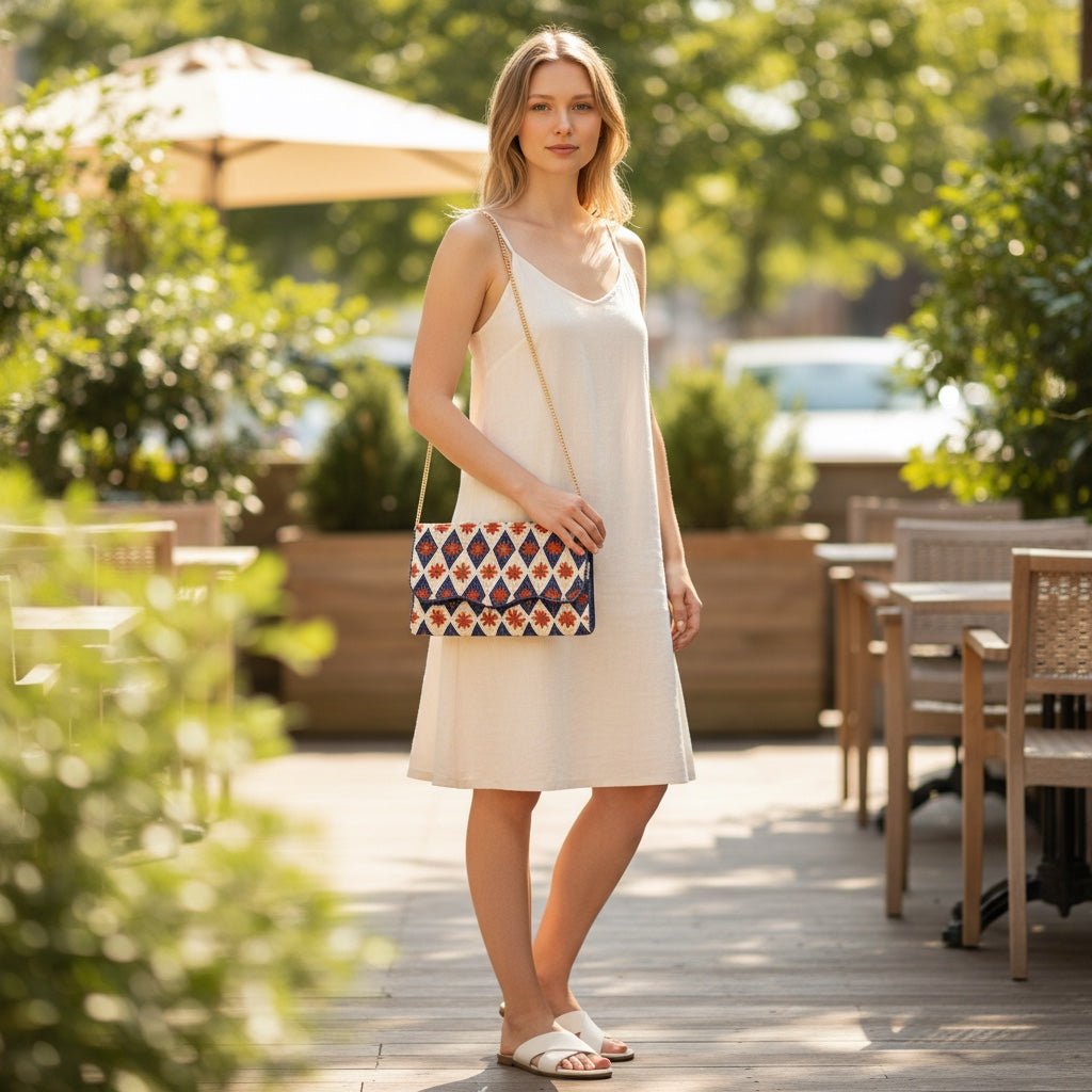 Woman wearing a white dress holding a JOYCO Golden Azure embroidered clutch with gold chain strap on a patio