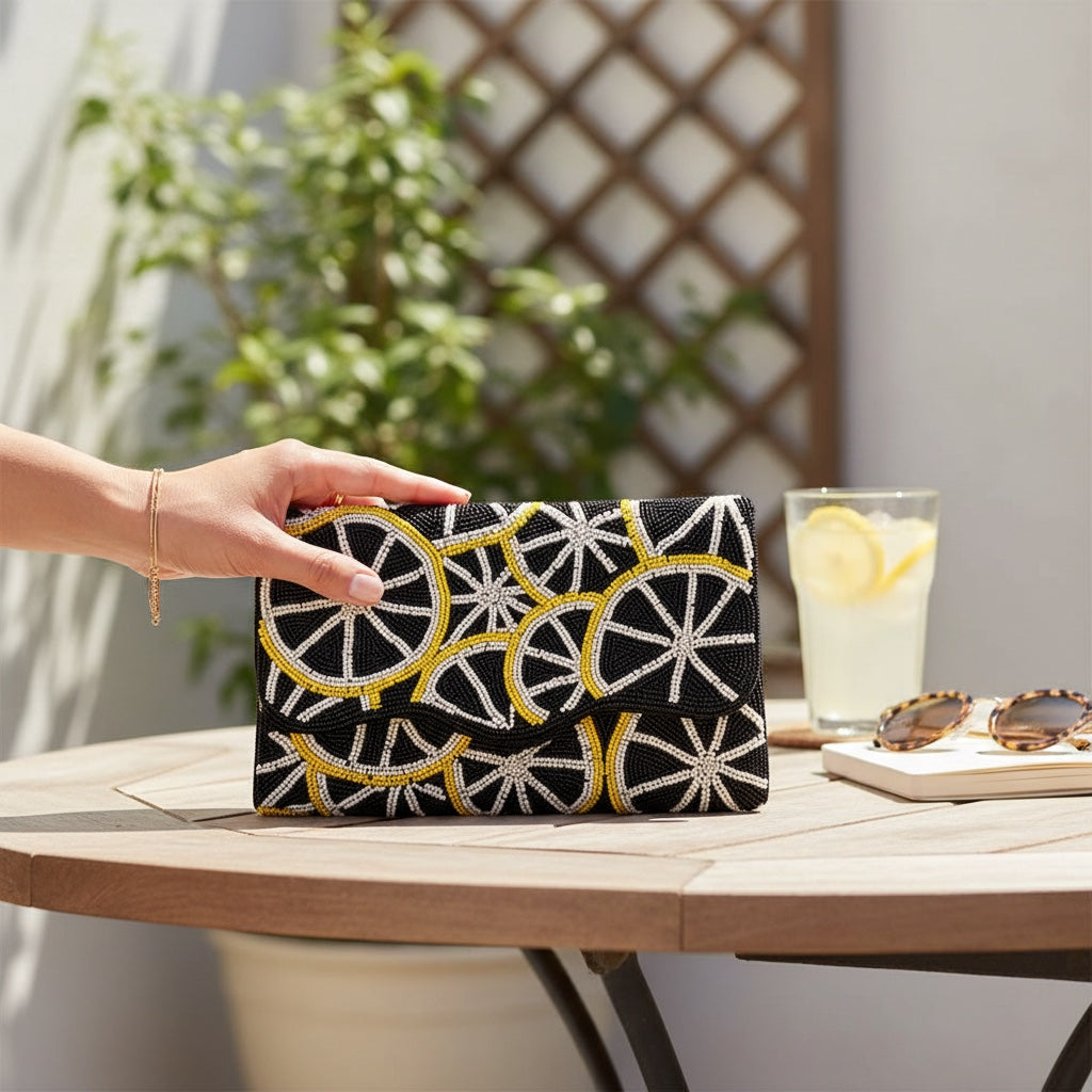 JOYCO Lemon Dolce clutch with black, yellow, and white beaded lemon slice embroidery on a wooden outdoor table