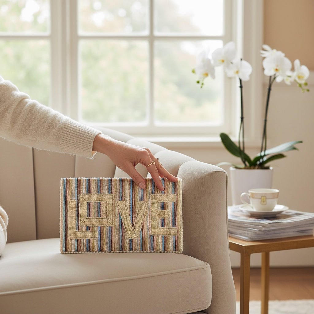 JOYCO Love Embroidered Clutch with striped pattern and gold lettering, held by a hand on a beige armchair.