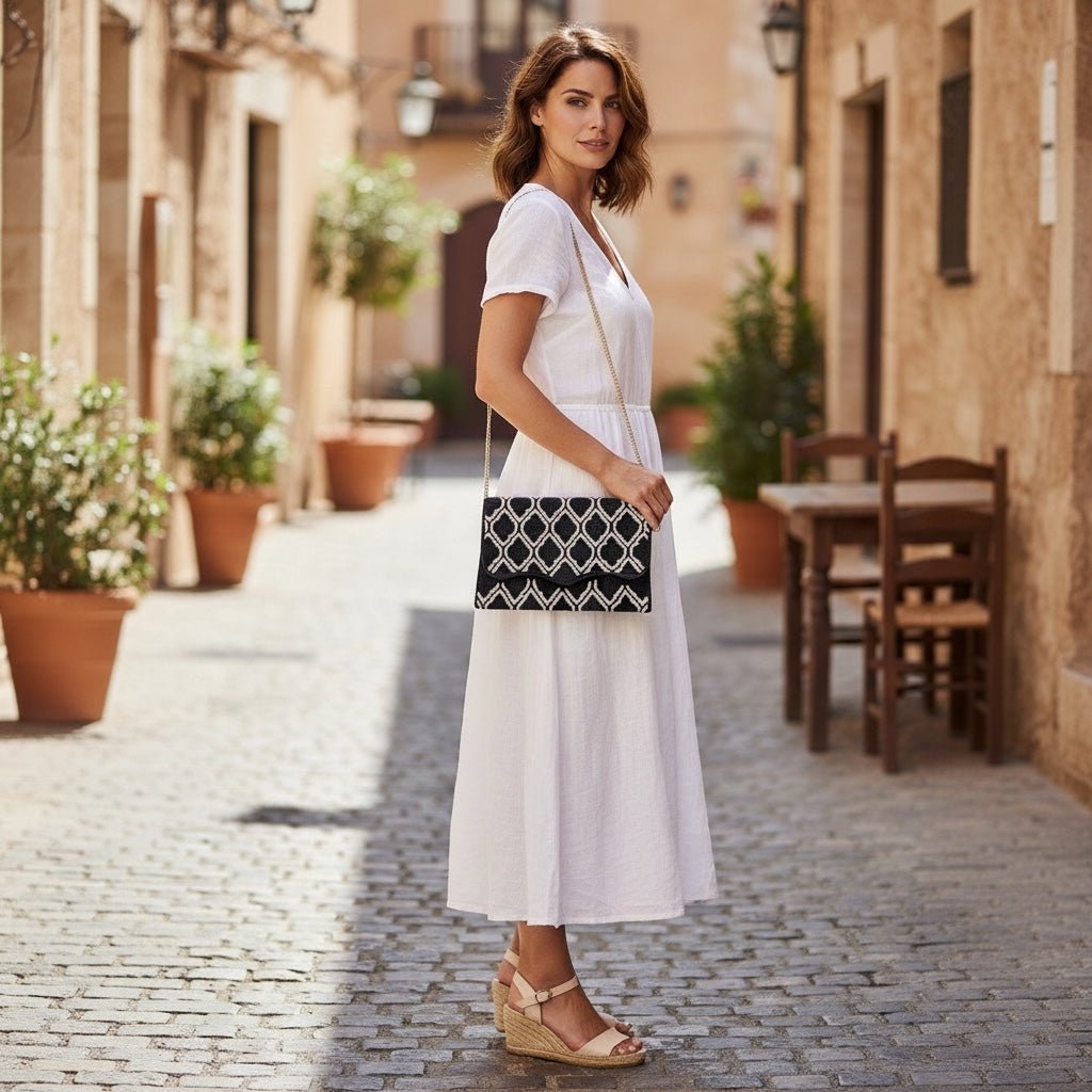 JOYCO Maison Noir embroidered clutch with geometric pattern worn by a woman in a white dress on a cobblestone street.