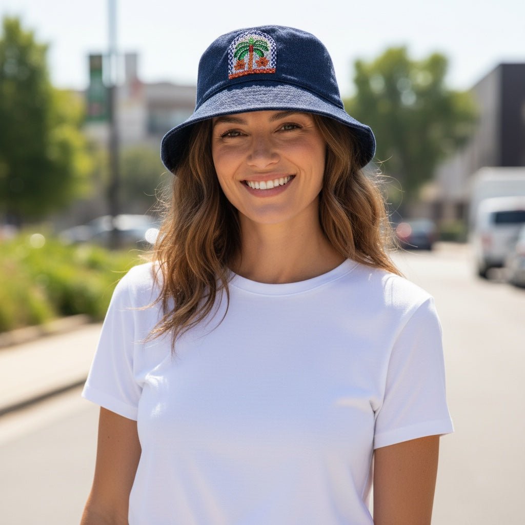 A smiling woman wearing a JOYCO navy blue bucket hat with a colorful palm tree embroidery design outdoors.