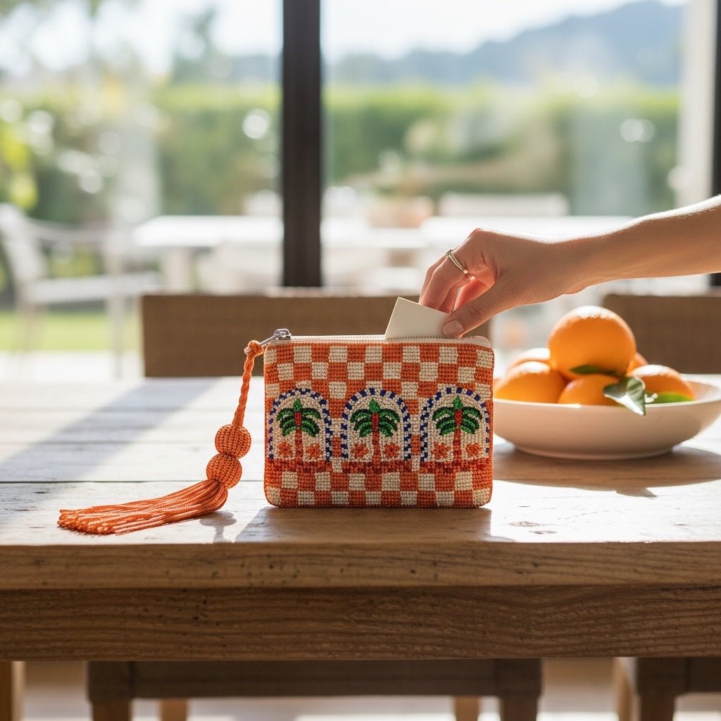 JOYCO Palm Mirage embroidered pouch with orange and white checkered pattern and palm tree design on a wooden table.