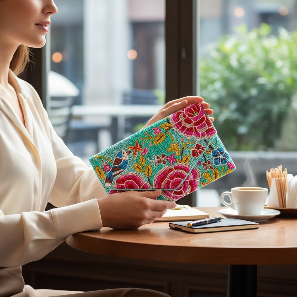 JOYCO Paloma clutch featuring vibrant floral and bird embroidery on a turquoise background held by a woman at a cafe.