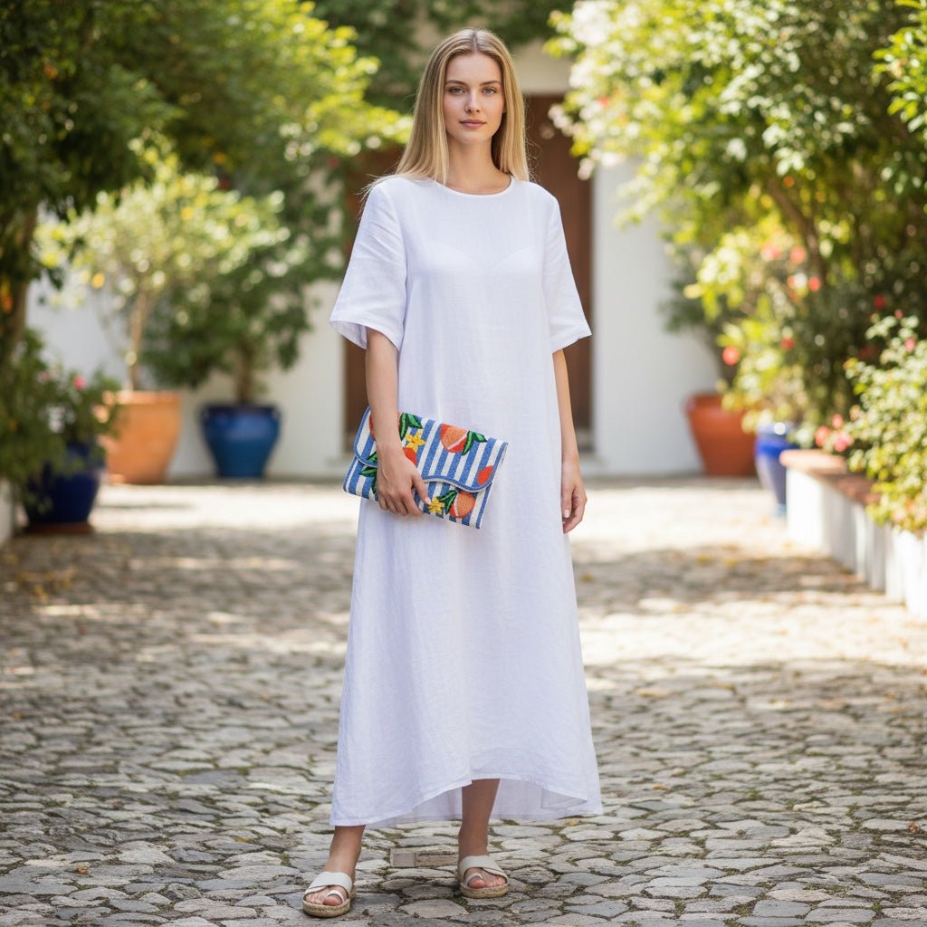 JOYCO Peach Riviera Embroidered Clutch with blue and white stripes and peach motifs held by a woman in a white dress