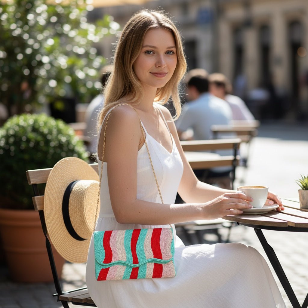 JOYCO Rainbow Embroidered Clutch with gold chain strap worn by a woman in a white dress at an outdoor cafe