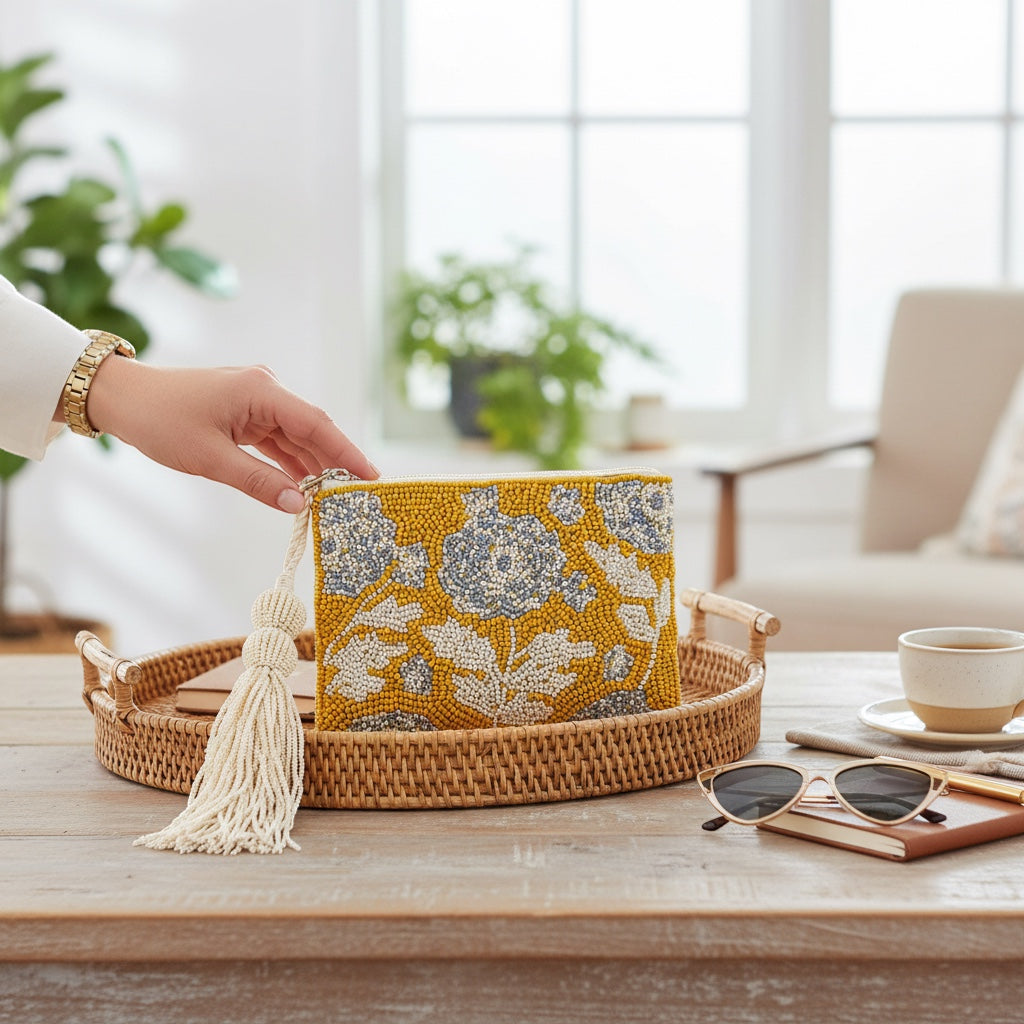 JOYCO Soleil Bloom embroidered pouch in yellow and white with a tassel, sitting on a rattan tray on a wooden table.