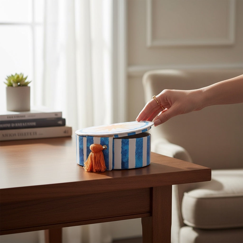 JOYCO Sun Jewellery Box in blue and white striped cotton linen with an orange tassel on a wooden table