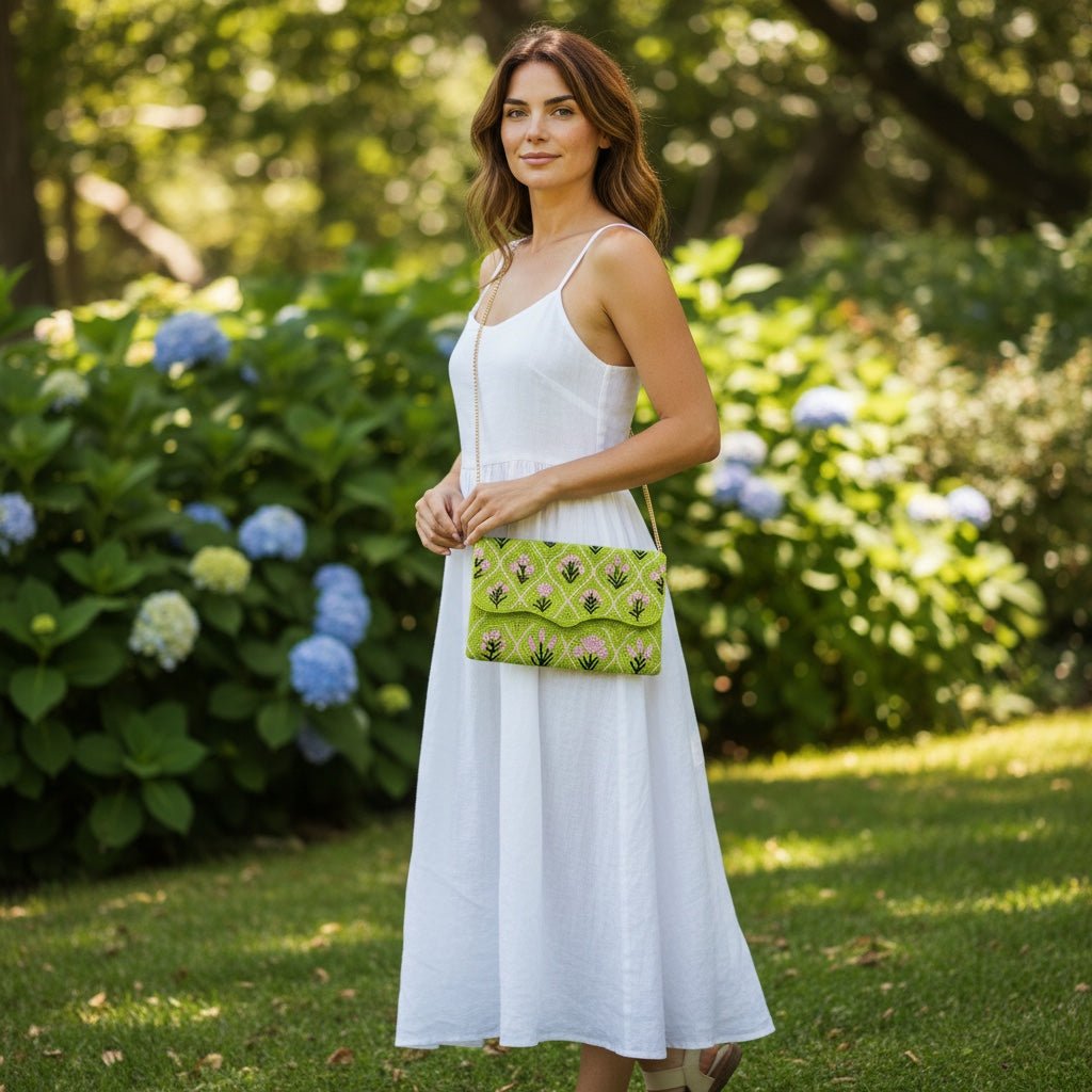 JOYCO Verdant Muse green embroidered clutch with floral pattern, worn by a woman in a white dress in a garden.